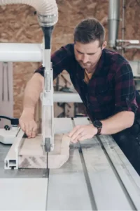 vue de face de l'artisan menuisier en train de réaliser des découpe de bois avec une machine.