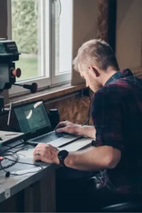 vu de 3/4 dos l'artisan menuisier en train de paramétrer la machine sur son ordinateur.